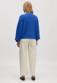 Blauwe gebreide trui met een relaxte pasvorm, lange mouwen en geribbelde manchetten, gecombineerd met witte wijde broek en zwarte instapschoenen.