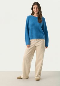 Blå ribbet striktrøje med lange ærmer, parret med cremede corduroy bukser med vide ben og beige slip-on sko. Simpel, afslappet pasform.