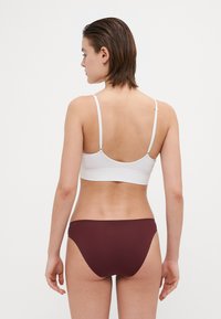 Bralet alb texturat cu bretele subțiri și chiloți bordeaux. Braletul are un spate rotund și margini fără cusături.
