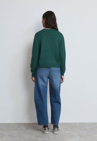 Suéter verde de punto con cuello redondo, combinado con jeans de denim azul sueltos. El atuendo se completa con zapatos plateados cubiertos de lentejuelas.