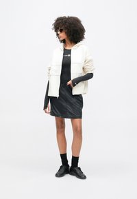 Λευκό μπουφάν με φερμουάρ και κουκούλα, μαύρο εφαρμοστό τοπ, μαύρη φούστα και μαύρα αθλητικά παπούτσια. Γυαλιά ηλίου ολοκληρώνουν το casual look. Ομαλές υφές.