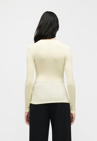 Ανοιχτό κίτρινο μακρυμάνικο τοπ με εφαρμοστή γραμμή και στρογγυλή λαιμόκοψη, κατασκευασμένο από απαλό, ελαφρύ υλικό, βλεπόμενο από πίσω.