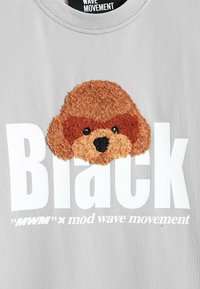 Camiseta gris con un aplique de la cara de un animal texturizado en marrón y beige. Gran texto blanco que dice "Black" con una marca más pequeña debajo.