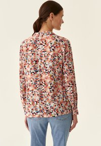 Langærmet blomsterbluse i bl�ødt stof med små pink, blå og gule blomster på en mørk baggrund, rund halsudskæring og lige kant.