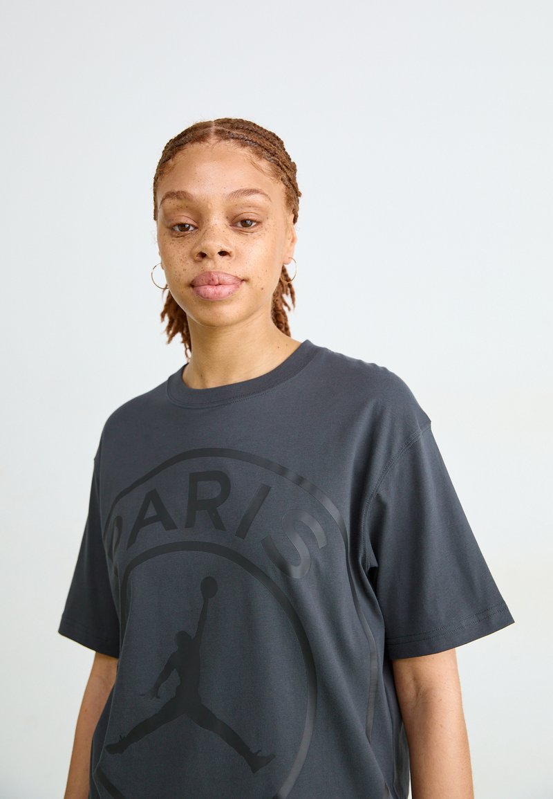Dunkelgraues, übergroßes T-Shirt aus weichem Stoff, mit einem großen schwarzen Grafikdesign des Paris-Logos und einer Silhouette einer springenden Figur.