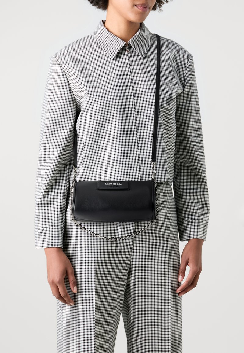 Black leather crossbody bag with a chain strap, featuring a smooth finish and a rectangular shape. Branded tag in white on the front.