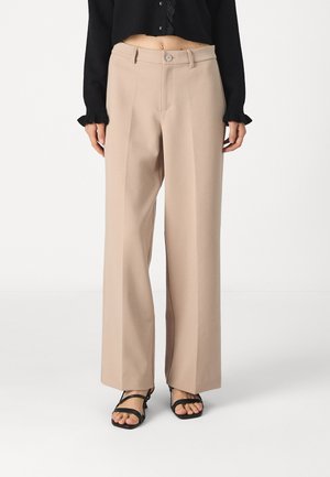 Beżowe spodnie z szerokimi nogawkami i wysokim stanem, noszone z czarnymi sandałami na paski oraz krótką czarną bluzką z długim rękawem z koronkową lamówką.