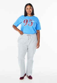 Blå bomuld T-shirt med stort "95" grafik, kombineret med lysegrå joggingbukser og bordeaux sneakers med lysebrune såler.