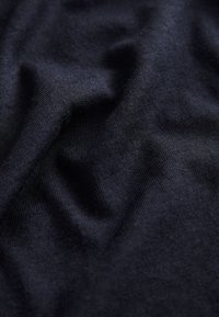 Temno modro bombažno blago z gladko teksturo, ki prikazuje nežne gube in fino rebrasto strukturo po celotni površini.