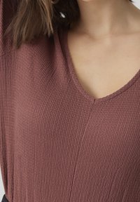 Top mauve melangiato con tessuto testurizzato, maniche corte e profondo scollo a V. Materiale leggero e leggermente elasticizzato.