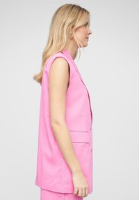 Blazer sans manches rose en tissu lisse, arborant un design à boutonnière simple avec deux poches avant et une coupe ajustée.