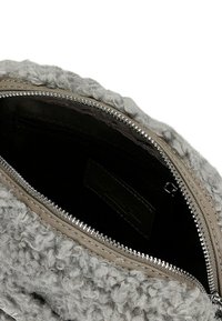 Nahaufnahme einer offenen grauen Tasche mit lockiger Wollstruktur, die einen silbernen Reißverschluss und eine schwarze Stoffinnentasche mit Reißverschluss hat.