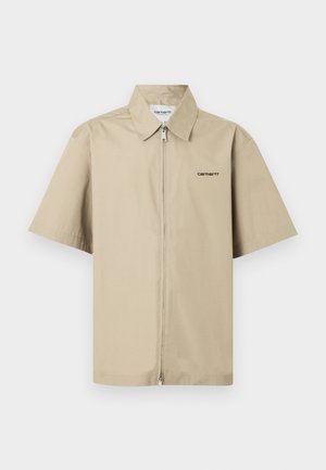 Smėlio spalvos trumpomis rankovėmis marškiniai su pilnu priekiu užtrauktuku ir maža juoda Carhartt logotipu kairėje krūtinės pusėje.