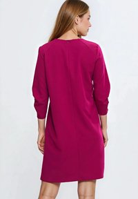 Różowa sukienka do kolan z rękawami o długości 3/4, zaokrąglonym dekoltem i dyskretnym zamkiem z tyłu. Gładka tkanina, minimalistyczny design.