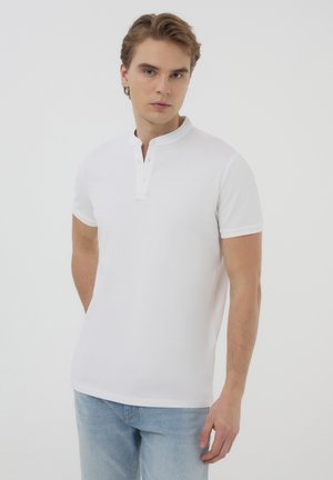 Polo shirt bianco a maniche corte con colletto alla cinese e pattina con tre bottoni. Il tessuto morbido, il design aderente e la trama liscia accentuano la semplicità.