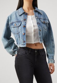 Ljusblå denimjacka med knäppningar, två bröstfickor och kort längd, matchad med svarta jeans. Slät yta, klassisk design.