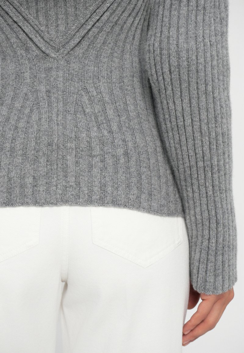 Gray ribbed knit sweater with a v-neck design, featuring a soft texture and fitted sleeves, paired with white pants showing rear pocket details.