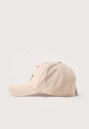 Béžová baseballová čepice s prohnutým kšiltem a nastavitelným páskem, položená na boku na čistém bílém pozadí.