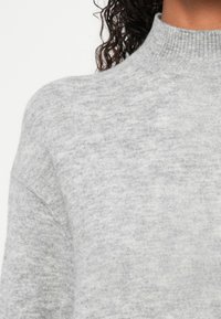 Maglione lavorato a maglia grigio chiaro con collo alto, realizzato in un morbido tessuto testurizzato. Presenta una vestibilità comoda e maniche scese.