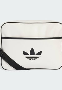 Borsa sintetica bianca con piping nero e tracolla regolabile. Presenta un logo Adidas nero e tre strisce orizzontali sul davanti.