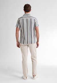 Korte mouw gestreepte shirt in blauwe, witte en beige stof met een kraag, gedragen met lichtbeige broek en witte sneakers.
