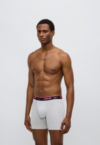 Γκρι ανδρικά εσώρουχα Nike boxer με μαύρη μέση που διαθέτει ροζ λογότυπο κειμένου· εφαρμοστή σχεδίαση, ομαλή υφή, με μήκος έως το μέσο του μηρού.