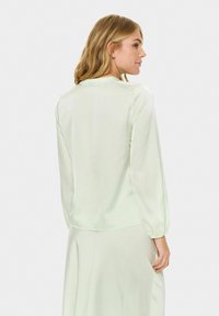 Světle zelená blůza s dlouhými, nabíranými rukávy a kulatým výstřihem. Vyrobena z hladké látky, s elegantním, minimalistickým designem.