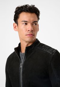 Schwarze Lederjacke mit Reißverschluss vorne, mit glatter Textur und Stehkragen, vor einem neutralen Hintergrund.