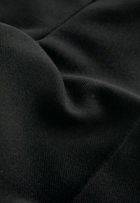 Tissu noir avec une texture douce et côtelée, présentant des plis et des courbes subtils. Le matériau est léger et flexible, idéal pour diverses applications.