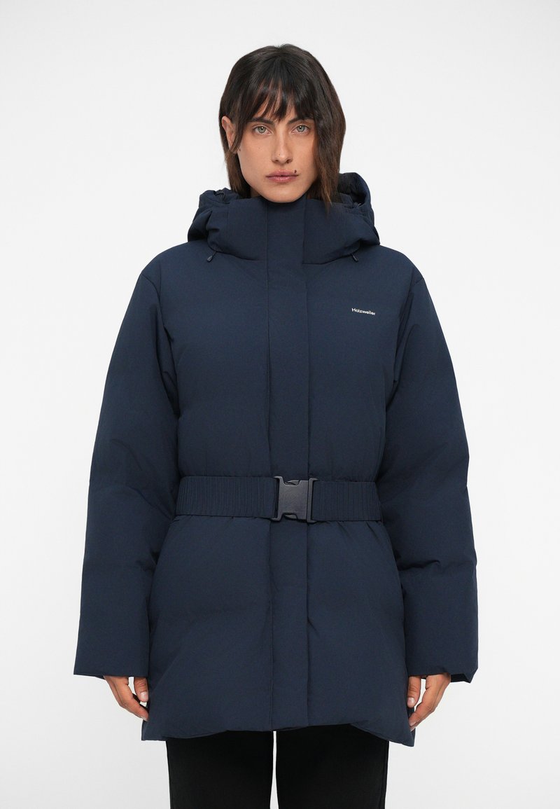 Doudoune bleu marine avec un col montant, une capuche ajustable et une large ceinture. Elle présente une texture lisse et des manches amples.