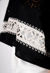 Black top with intricate white lace trim, featuring floral patterns and openwork details. The fabric is lightweight and textured.