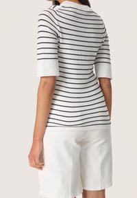 Top de punto blanco con rayas horizontales en azul marino, mangas cortas y escote redondeado. Combinado con pantalones cortos blancos, mostrando un ajuste casual.
