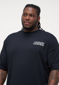 Black short-sleeve t-shirt made of cotton, featuring a white "LEGENDS" logo on the left chest and a relaxed fit design.