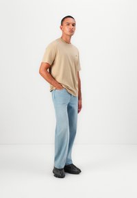 Beige pamut póló rövid ujjal, világoskék, bőszárú farmerral párosítva. Az outfit fekete sportcipővel van kiegészítve.