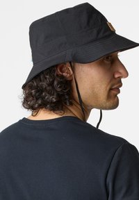 Black bucket hat with a wide brim, textured fabric, and a leather brand tag. Features adjustable chin strap for secure fit.
