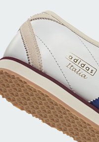 White leather sneaker with beige and navy accents, featuring a textured rubber sole, suede detailing, and a gold "adidas Italia" logo.