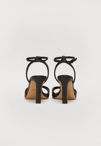 Černé sandály na vysokém podpatku s tenkými kotníkovými pásky, otevřenou patou a designem s odkrytými prsty. Mají hladký kožený povrch a elegantní stiletto podpatek.