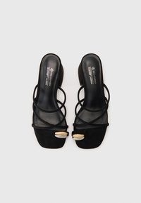 Sandalias de ante vegano negro con tiras cruzadas, punta cuadrada y un pequeño tacón cuadrado con detalles metálicos.