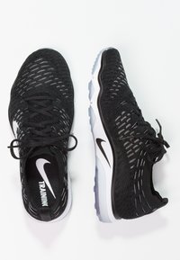 Scarpe da allenamento nere con tomaia in maglia, design con lacci e accenti bianchi e grigi a contrasto. Presentano un'unità sole ad aria visibile.
