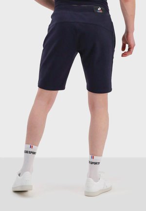 Pantalones cortos deportivos navy con un diseño ajustado, textura suave y una cinturilla ancha. Combinados con zapatillas blancas y calcetines tobilleros con un logo.