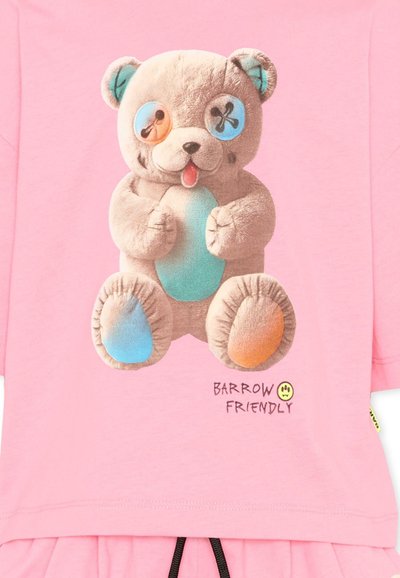 Orsetto di peluche con occhi a bottone disallineati, uno blu e uno arancione, su tessuto rosa, con la scritta "Barrow Friendly" e una piccola faccina gialla sorridente.