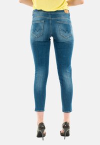 Jeans skinny blu con una finitura sbiadita, due tasche posteriori con cuciture a forma di V e una vita alta. Abbinati a tacchi alti neri.