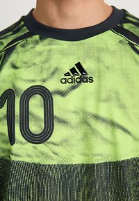 Nærbilde av en neon grønn og svart Adidas sportsdrakt med nummer 10 og svart rund hals på en person.