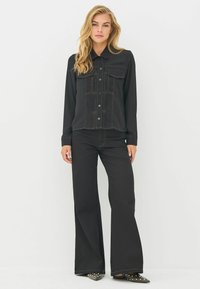 Sort denim langærmet skjorte med knaplukning, to brystlommer og kontrasterende syninger; parret med sorte brede bukser.