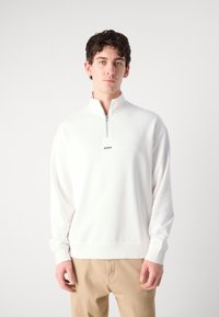 Hvitt kvart-glidelås sweatshirt laget av mykt stoff, med ribbestrikkede mansjetter og hem; logoen "HUGO" trykt på brystet.