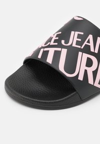 Sandale à glissière noire avec semelle texturée et large bride ornée de lettres roses en relief formant le mot "JUICE JEAN" ainsi que de petites formes de cœur.