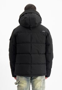 Zwarte pufferjack met een capuchon, uitgerust met doorgestikte panelen, een logo aan de achterkant en een gladde, matte textuur. Ontworpen voor warmte en comfort.