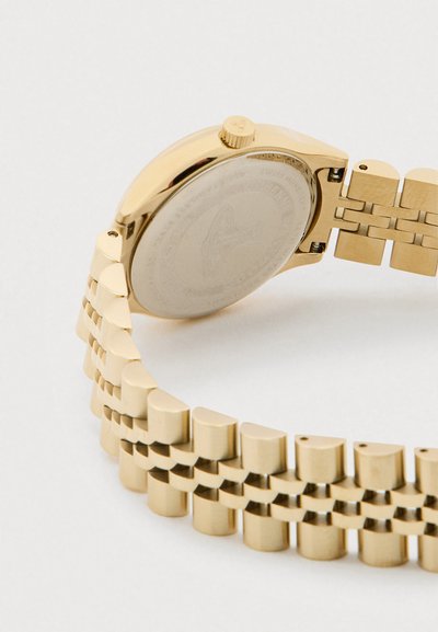 Zelta rokas pulkstenis ar metāla saišu siksnu, attēlots aizmugures korpuss un pulksteņa kronis uz vienkārša balta fona.