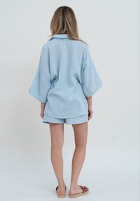 Chemise surdimensionnée en mélange de coton bleu clair avec des manches courtes et un short assorti, présentant une finition texturée et une coupe décontractée.