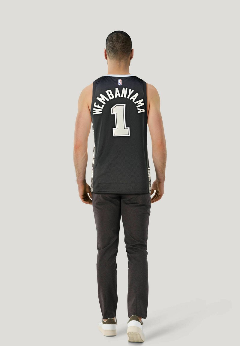 Schwarzes NBA-Trikot mit "WEMBANYAMA" und "#1" in weißem Text, getragen mit dunklen Hosen und weißen Sneakern. Aus Mesh-Material und sportlichem Schnitt.
